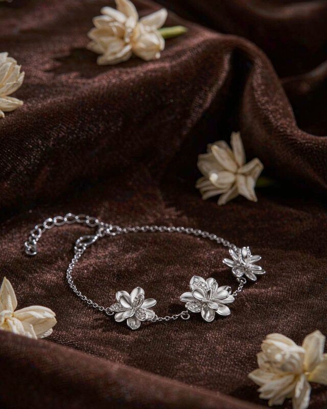 Silver jasmine flower bracelet with three sculpted blossoms on brown velvet