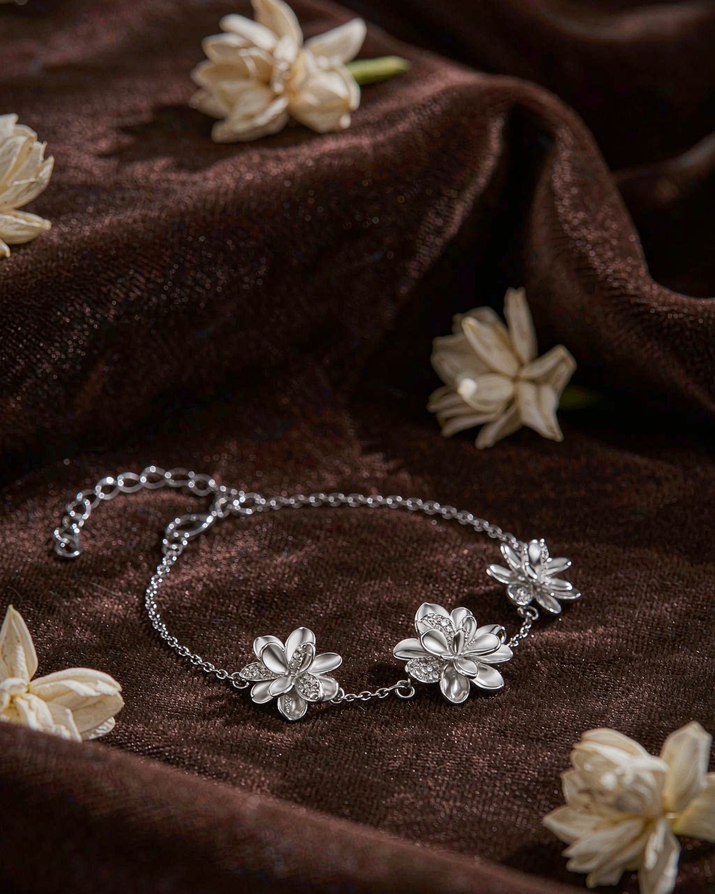 Silver jasmine flower bracelet with three sculpted blossoms on brown velvet