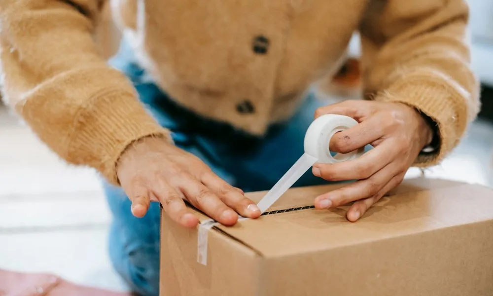 Hands sealing a parcel with packing tape before dispatch