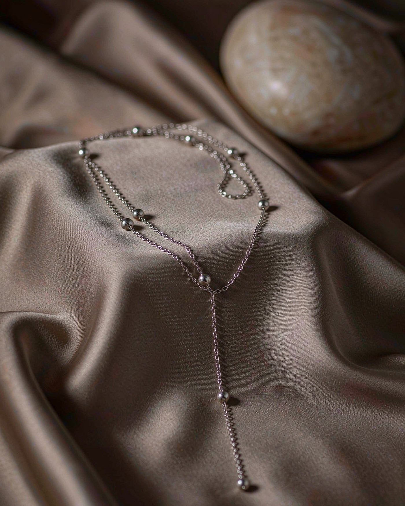 Silver beaded lariat necklace with a long beaded drop on taupe silk